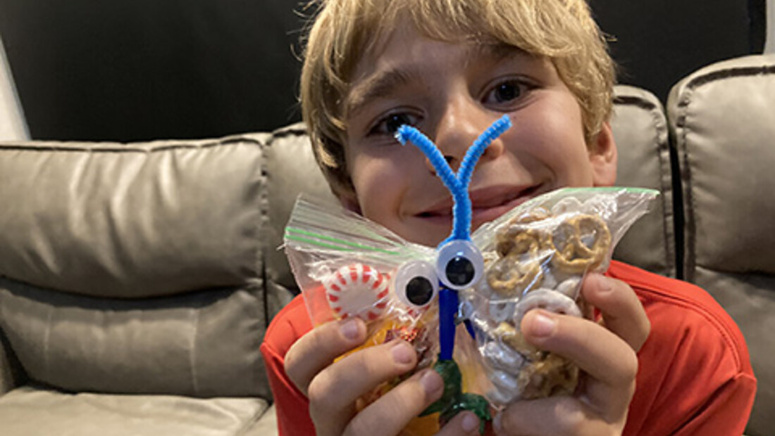 Smiling boy holding a handmade butterfly snack-bag craft with googly eyes, pretzels, and peppermints